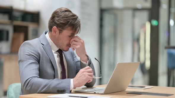 Stressed Businessman with Laptop Having Headache in Office 