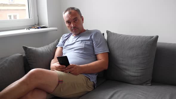 Mature Man Using Mobile Phone at Home on the Couch