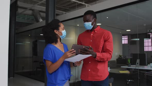 Diverse race male and female business colleagues wearing face masks discussing over tablet