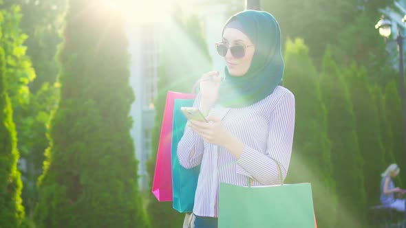 Young Muslim Woman in Hijab Bags in His Hands After Shopping Using the Phone Sunflare