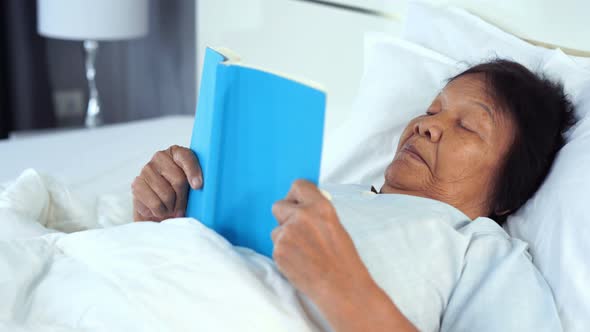 old woman reading a book on bed in bedroom