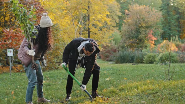 Group People Volunteers Eco Activists Plants Tree in Autumn Park Young Woman and Guy with Shovel