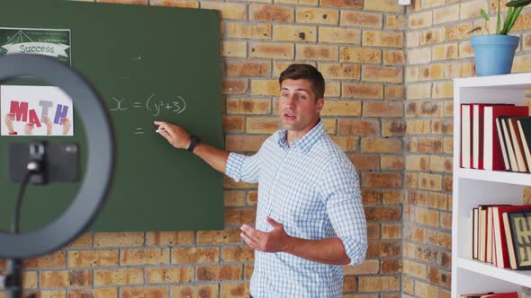 Caucasian male maths teacher standing at blackboard giving an online lesson to camera