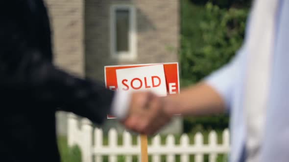 Two Man Shaking Hands on Background of Sold Signboard Successful House Buying