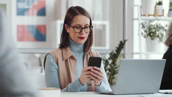 Businesswoman Surfing the Net on Smartphone at Office Desk