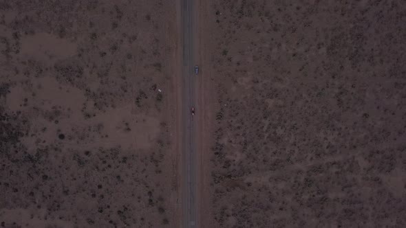 AERIAL: Birds View Flight Over Lonely Abandoned Desert Road with Red Car Driving in the Distance 