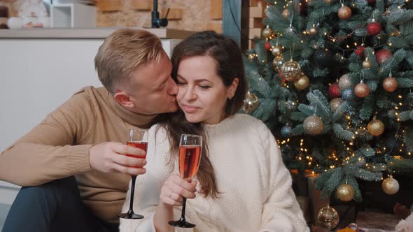 Couple Sitting and Hugging Near the Christmas Tree and Drinking Champagne.