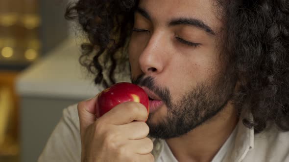 Arabian Man with Kinky Hair Enjoys Eating Apple in Kitchen