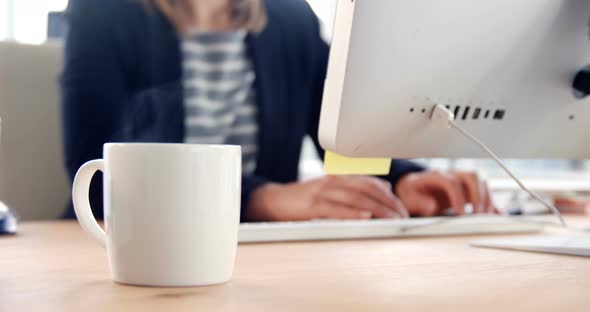 Close-up of coffee mug while businesswoman working over computer