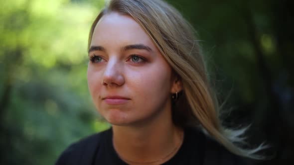 Slow Motion Shot of a beautiful blonde female sitting in the mountains and she is staring off in the