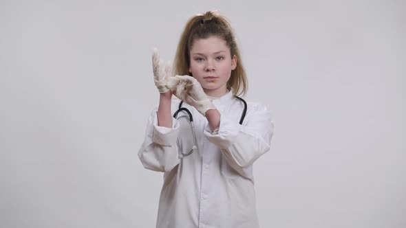 Confident Serious Caucasian Girl in White Doctor Gown Putting on Disposable Glove Looking at Camera