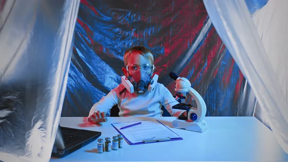 A Child Scientist Wearing a Respirator and Goggles Works in the Lab with a Tablet