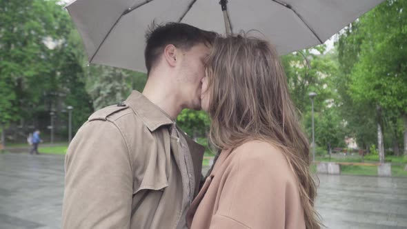 Close-up Side View of Loving Couple Kissing Under Umbrella on Rainy Day. Portrait of Happy Romantic