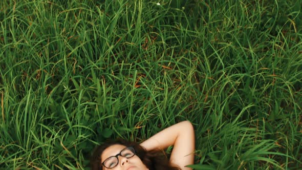 Girl in a flowered dress lies in tall grass.