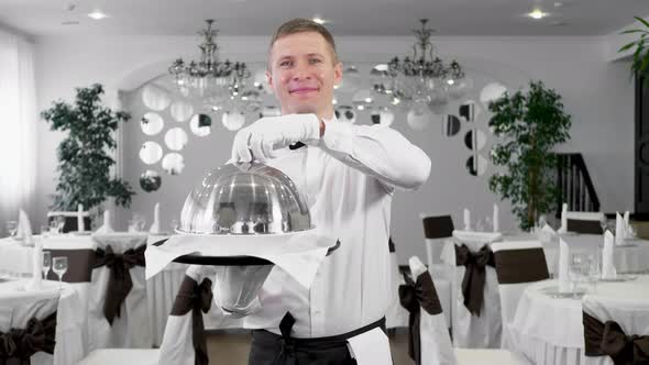 Male Waiter Opens the Lid of a Tray with a Hot Dish