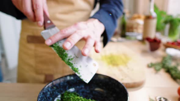 Male Chef Removing Chopped Parsley from Knife Blade