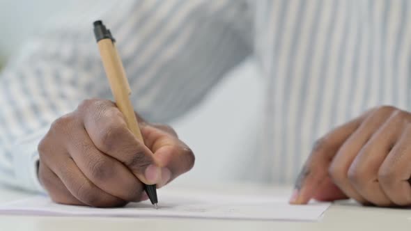 Close Up of African Man Writing on Paper with Pen