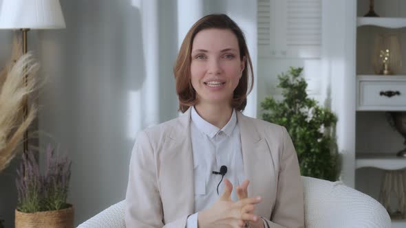 Smiling young woman, blogger, vlogger, influencer, sitting at home, talking, looking at the camera