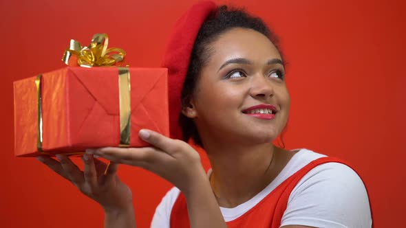 African American Woman Shaking Giftbox Trying to Guess What Is Inside, Present