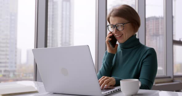 Young business woman talking on the phone while working on laptop at workplace in office