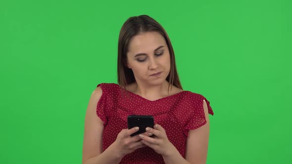 Portrait of Tender Girl in Red Dress Is Angrily Texting on Her Phone. Green Screen