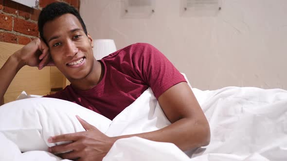 Happy African Man Relaxing in Bed Smiling While Looking in Camera