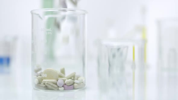 Panning view of pill dropping to glass container