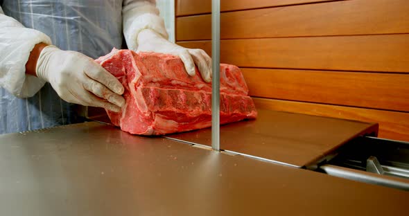 Butcher cutting meat on meat cutting machine in shop