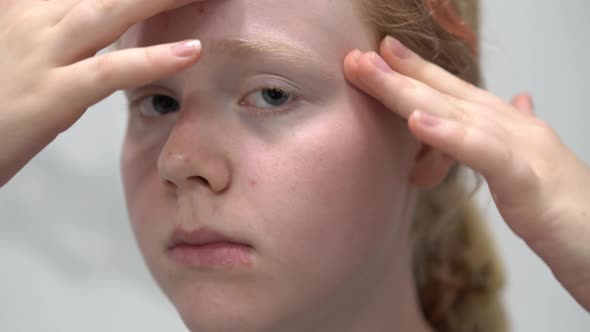 Teenage Girl with Problem Skin Examines Her Face in the Bathroom Mirror