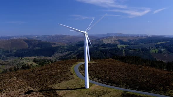 Two wind turbines lined up spinning their blades in the mountains with small green forests of trees