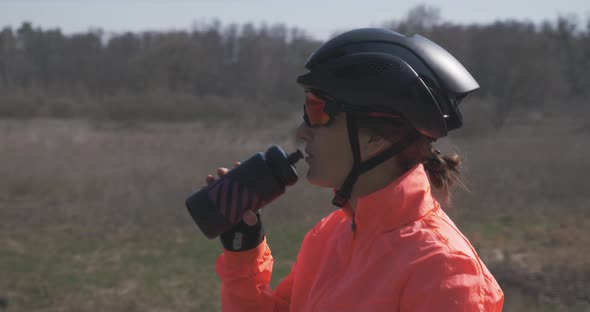 Portrait of woman cyclist in helmet and sunglasses is drinking water from bottle. Cycling hydration