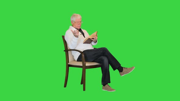 White-haired Senior Man Reading a Book To Camera on a Green Screen, Chroma Key.