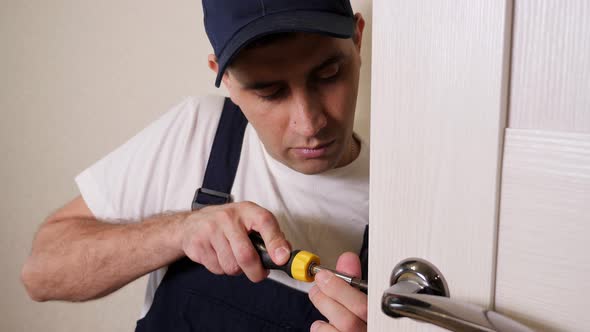 Portrait of Young Locksmith Workman in Blue Uniform Installing Door Knob