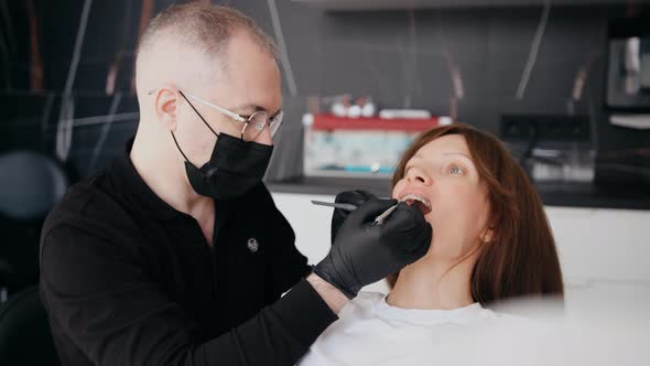 A Professional Dentist in a Protective Mask Works with a Patient in the Clinic