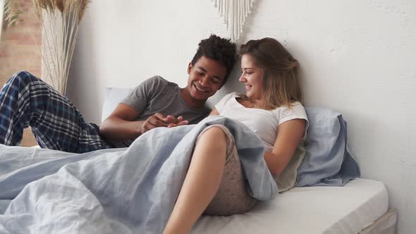 Young Cute Multiethnic Couple Lying in Bed and Talking