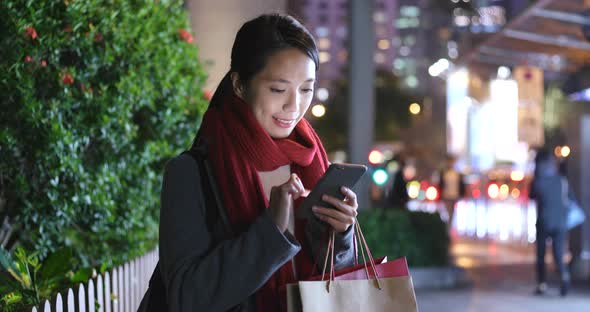 Woman use of smart phone in city at night and hold with shopping bag