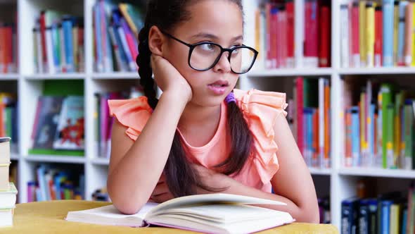 Thoughtful schoolgirl sitting on table in library at school