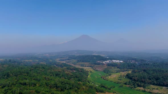 Grabag green valley with Sumbing and Sindoro mounts shrouded in fog in background. Aerial forward