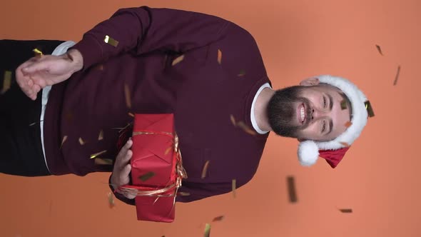 Man in santa claus hat holding gifts and tossing confetti