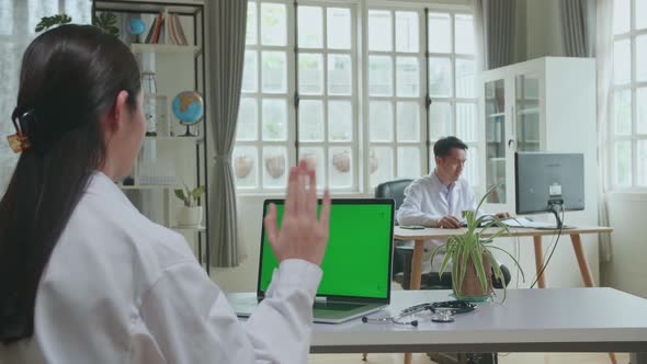 Asian Woman Doctor Having Video Conference On Laptop With Mock Up Green Screen Display In Workplace