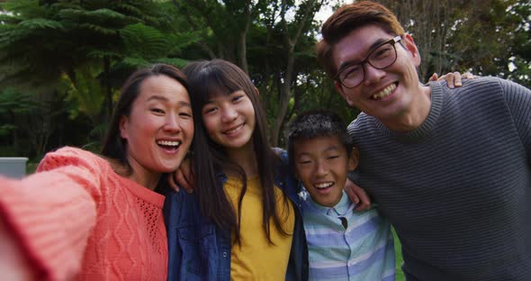 Happy asian mother taking selfie with happy husband,son and daughter in garden