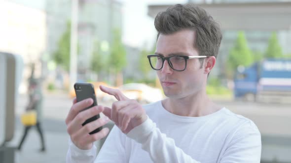 Young Man Browsing Internet on Smartphone Outdoor