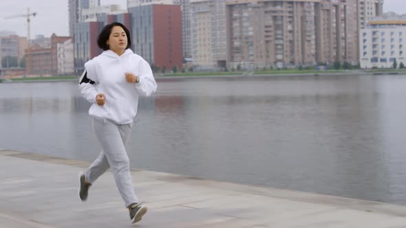 Asian Woman in Sportswear Running along Urban Riverside