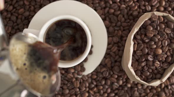 Hot Fresh Americano Is Poured Into Cup Against The Background Of Roasted Arabica Coffee Beans