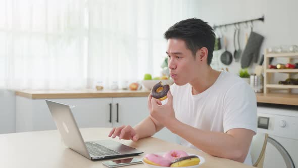 Asian business man eating unhealthy junk food while working from home.