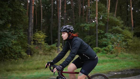 Young Woman Road Biker Wearing Protective Sport Helmet Riding Bicycle on Track in Autumn Forest