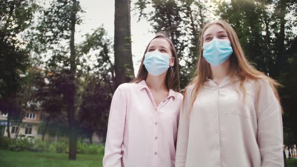 Portrait of two friends in medical masks,happy girls take off protective masks smiling and hugging.