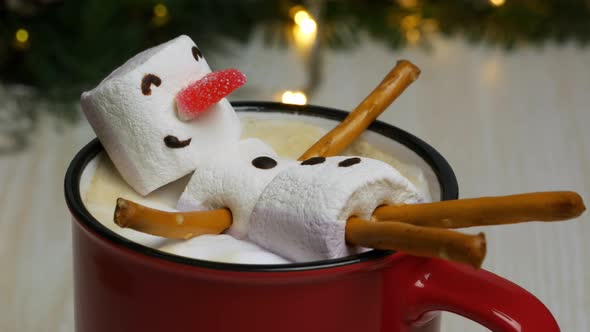 Marshmallow Snowman Basking in a Coffee Mug. Hot New Year's Drink on Background of Blinking Lights