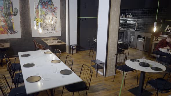 Pan of Interior of Modern Restaurant Where Owner Sits Alone at Table