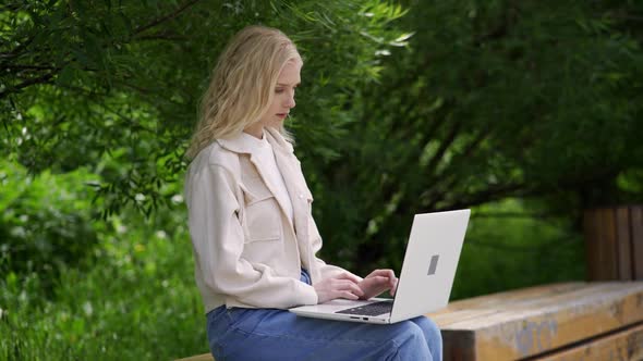 A Young Female Student is Sitting on a Park Bench with a Laptop